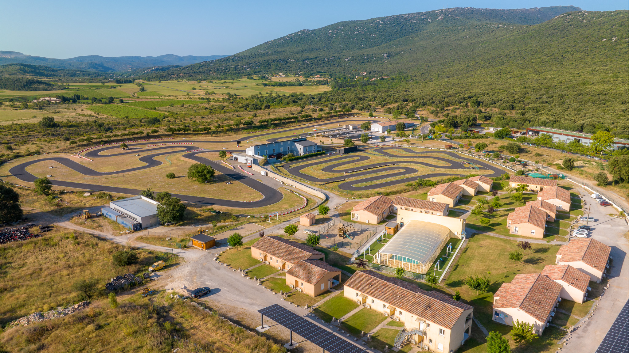 Vue aérienne de la Résidence du Parc à Brissac Cévennes, montrant les différentes zones de loisirs, y compris le karting, la piscine, le mini-golf et les hébergements.